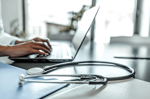 close up of hands typing on laptop next to a stethoscope 